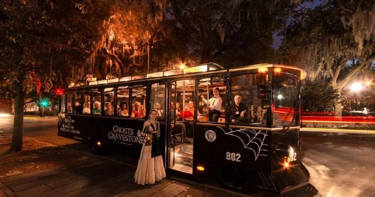 The black Ghosts and Gravestones trolley at night with a costumed guide on a trolley ghost tour in Savannah GA