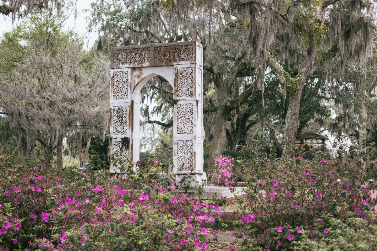 An ornate arch and azaleas in Bonaventure Cemetery, seen on a daytime Savannah GA cemetery tour by golf cart